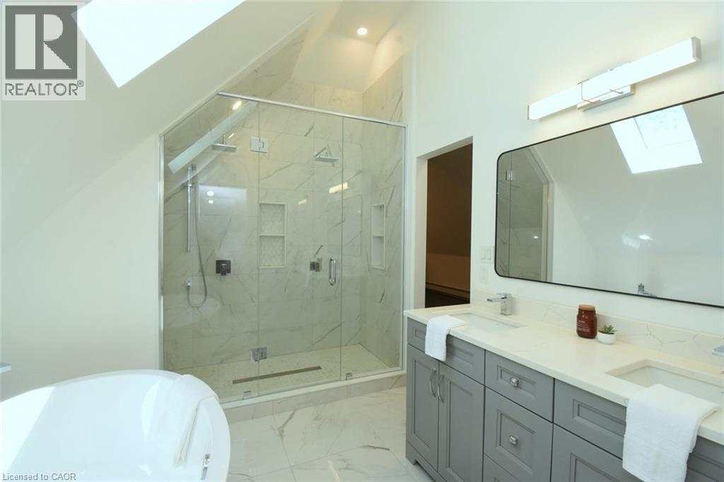 Spacious bathroom featuring a dual vanity with light gray cabinetry, a large walk-in shower with glass enclosure and built-in niches, and a freestanding soaking tub - 89 Lynden Road, Lynden, ON