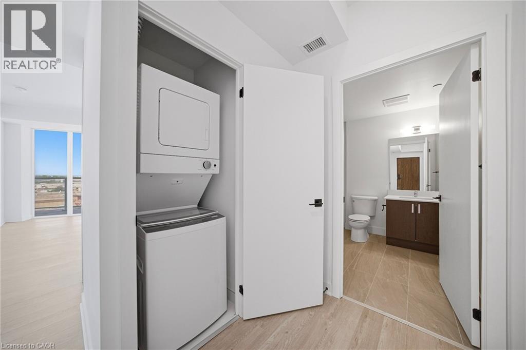 Integrated laundry closet featuring a stacked white washer and dryer unit - 2782 Barton Street E Unit# 516, Hamilton, ON - Indoor Photo Showing Laundry Room