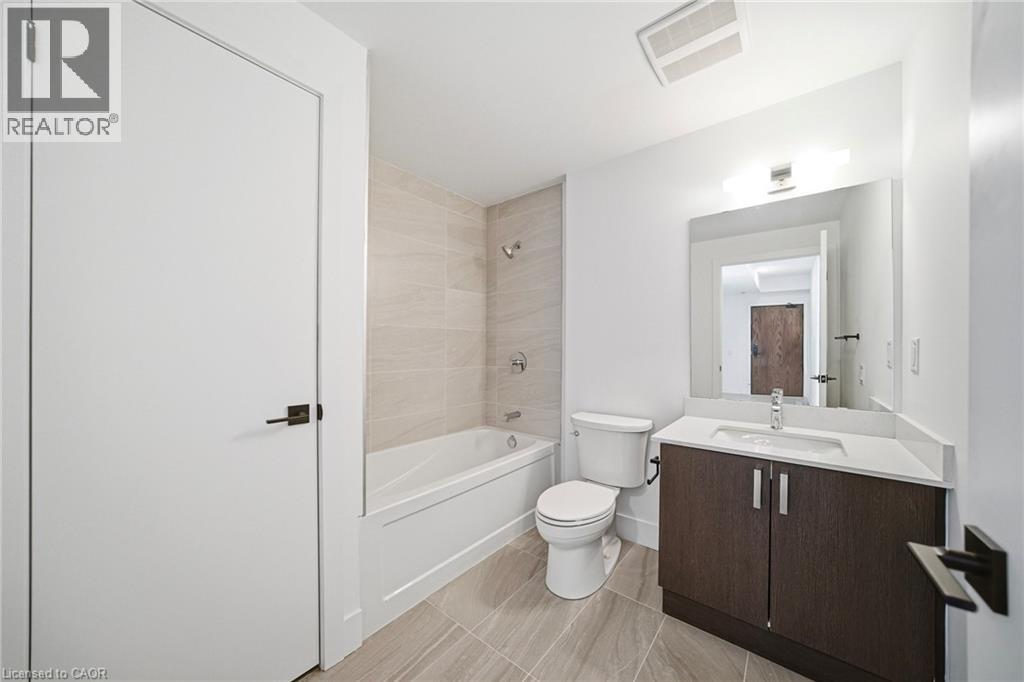 Bathroom featuring a white bathtub with tiled surround, a toilet, and a vanity with a white countertop and dark wood-finish cabinetry - 2782 Barton Street E Unit# 516, Hamilton, ON - Indoor Photo Showing Bathroom