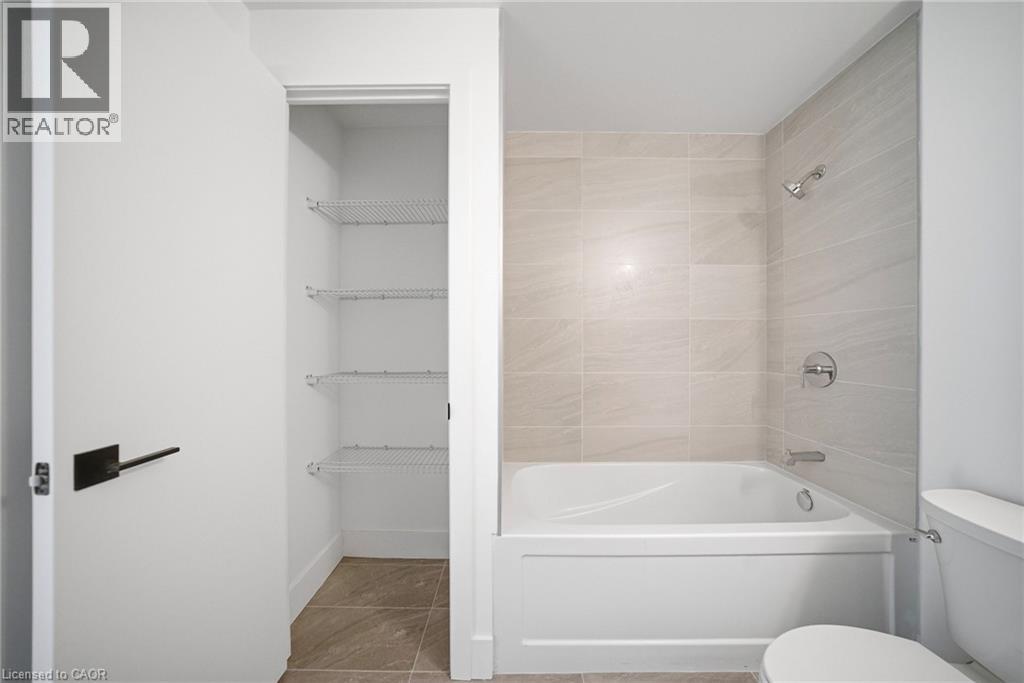 Full bathroom featuring a white porcelain tub, light-toned tile surround, chrome fixtures, and a white toilet - 2782 Barton Street E Unit# 516, Hamilton, ON - Indoor Photo Showing Bathroom