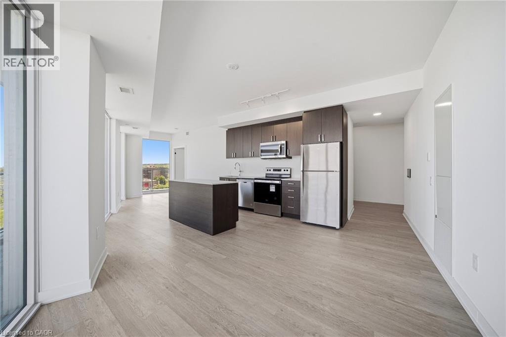 Open concept kitchen featuring dark wood cabinetry, stainless steel appliances, and a central island with a solid surface countertop - 2782 Barton Street E Unit# 516, Hamilton, ON - Indoor Photo Showing Kitchen