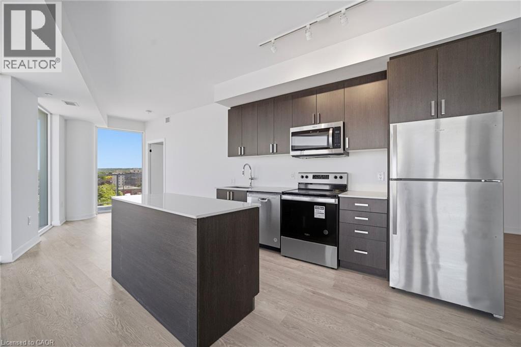 Modern kitchen featuring an island with a light-toned countertop, wood-finish flooring, and dark wood-finish cabinetry - 2782 Barton Street E Unit# 516, Hamilton, ON - Indoor Photo Showing Kitchen