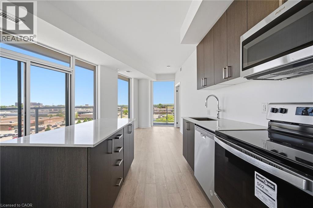 Contemporary kitchen featuring a full suite of stainless steel appliances, dark wood-finish cabinetry, and light-toned countertops - 2782 Barton Street E Unit# 516, Hamilton, ON - Indoor Photo Showing Kitchen With Upgraded Kitchen