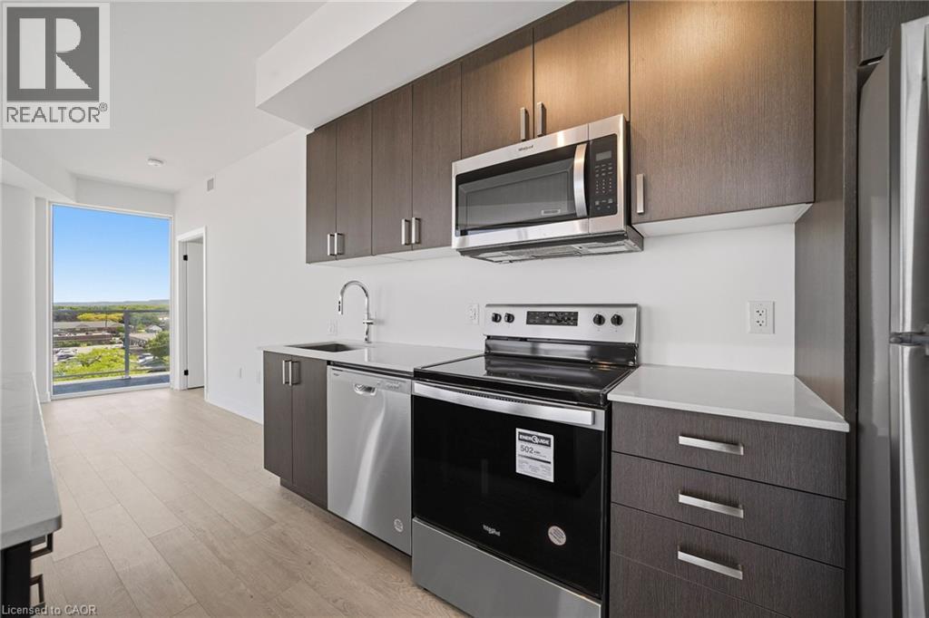 Contemporary kitchen featuring dark wood-finish cabinetry, stainless steel appliances, and light-toned countertops - 2782 Barton Street E Unit# 516, Hamilton, ON - Indoor Photo Showing Kitchen With Upgraded Kitchen