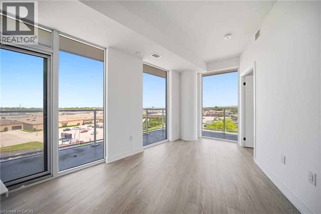 Bright interior space with expansive floor-to-ceiling windows, light wood-finish flooring, white walls, a balcony with a glass railing, and a modern ceiling light fixture - 2782 Barton Street E Unit# 516, Hamilton, ON - Indoor