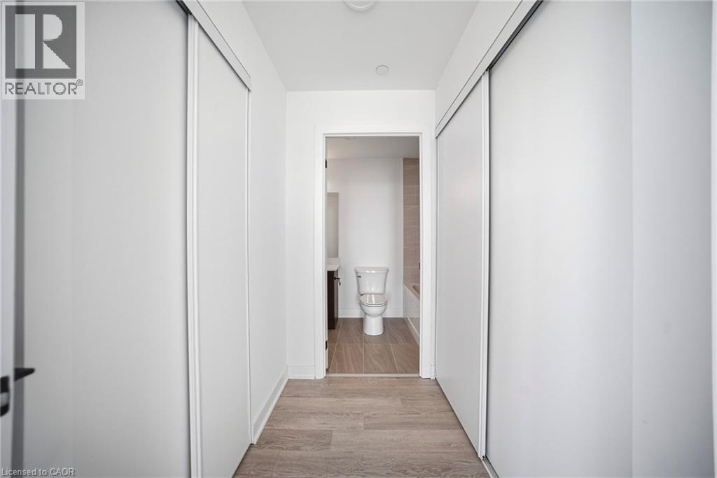 Hallway featuring light wood-finish flooring, white walls, and two sets of sliding closet doors - 2782 Barton Street E Unit# 516, Hamilton, ON - Indoor Photo Showing Other Room