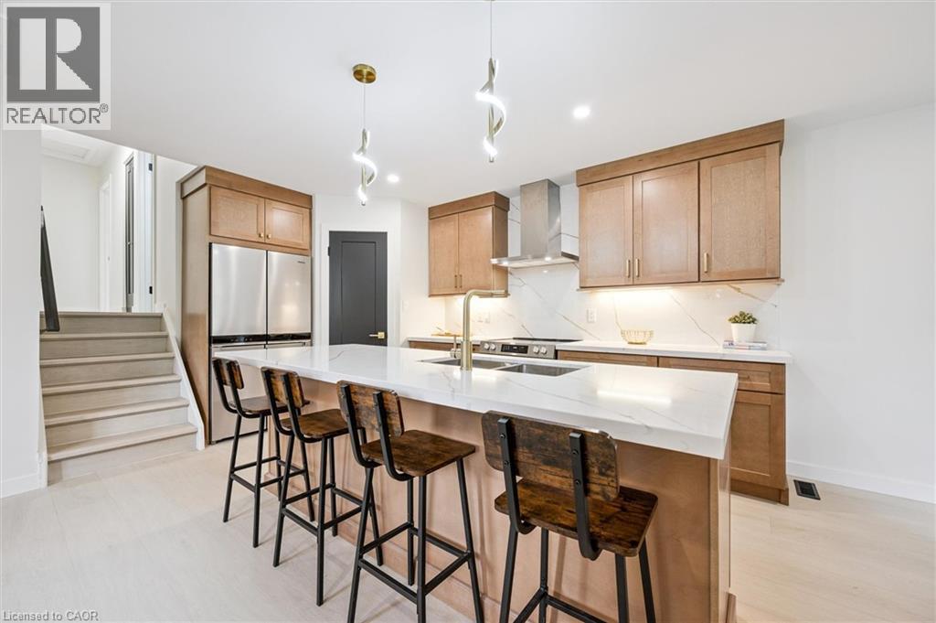 Kitchen featuring freestanding refrigerator, light stone countertops, tasteful backsplash, hanging light fixtures, and a breakfast bar - 459 Drummerhill Crescent, Waterloo, ON - Indoor Photo Showing Kitchen