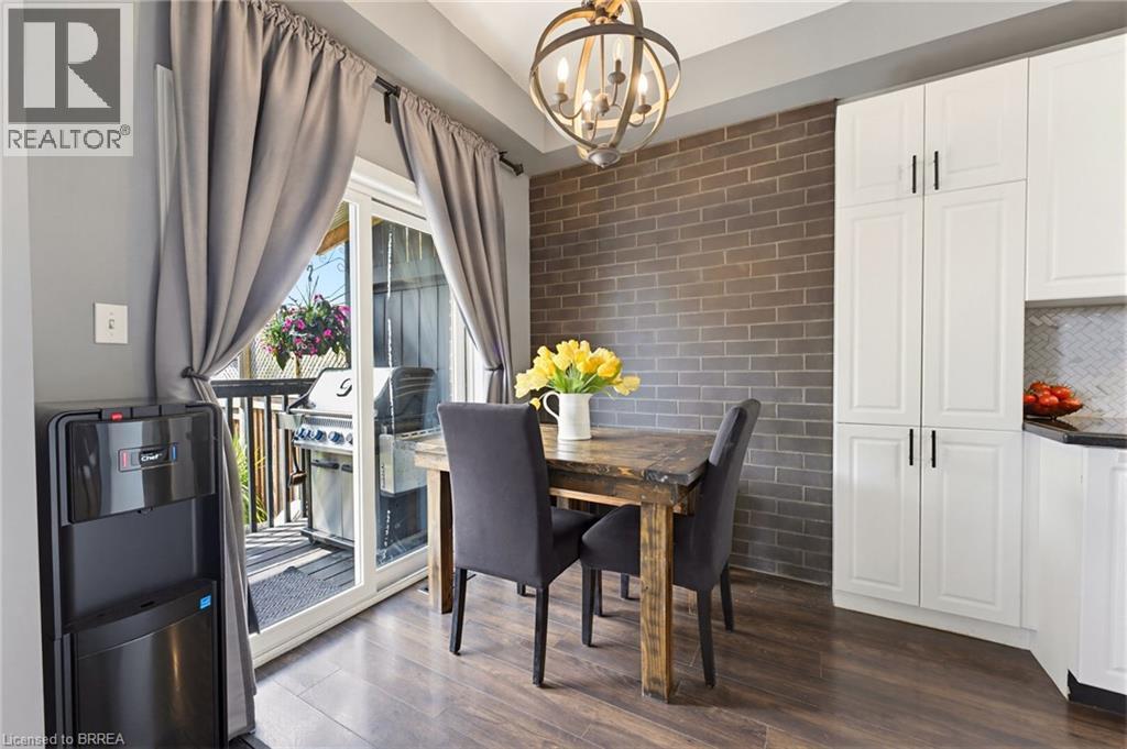 Dining area with wood-finish flooring featuring a brick-accented wall and a direct-access sliding glass door to an outdoor deck - 100 Chester Drive Unit# 16, Cambridge, ON - Indoor Photo Showing Dining Room