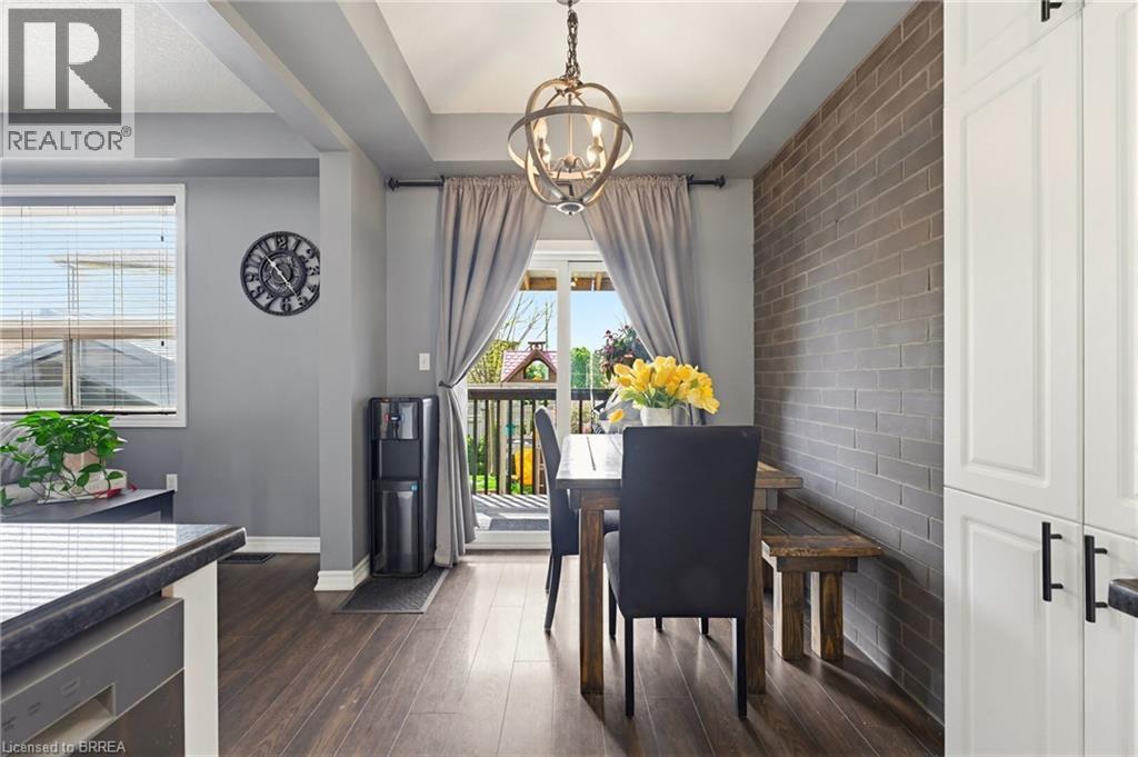 Dining area featuring wood-finish flooring, a tray ceiling with an overhead light fixture, a brick accent wall, and white built-in cabinetry with dark hardware - 100 Chester Drive Unit# 16, Cambridge, ON - Indoor Photo Showing Dining Room