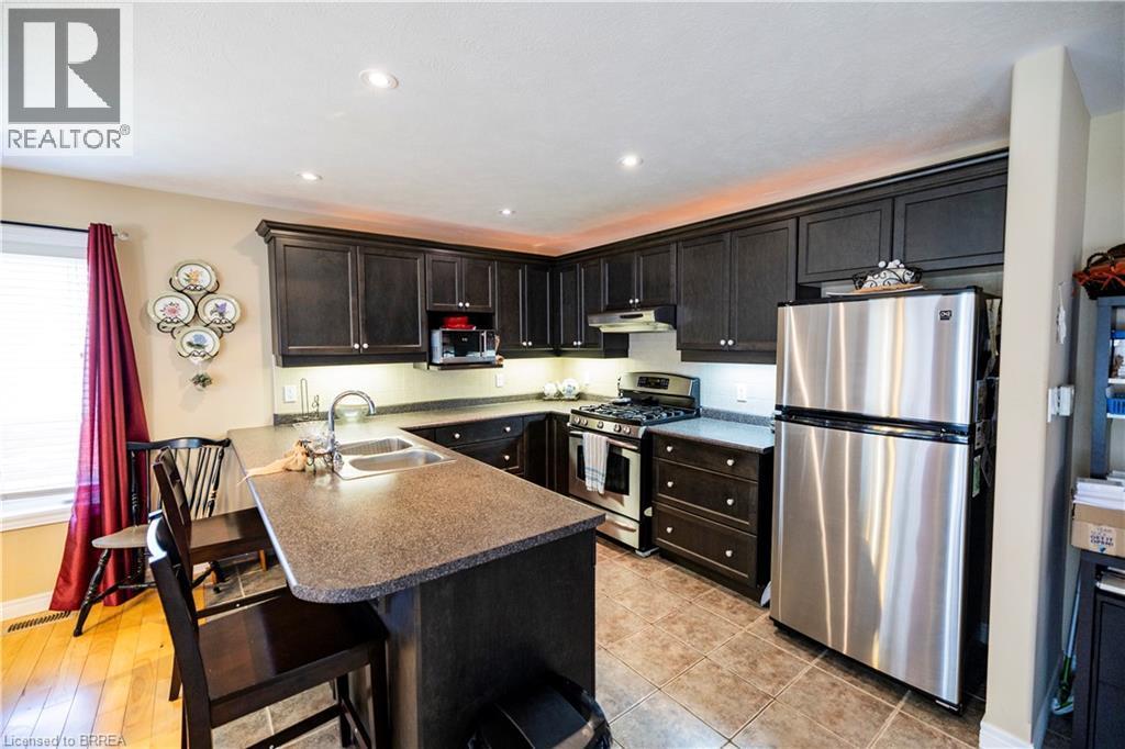 Kitchen featuring dark wood cabinetry, stainless steel appliances, a double basin sink, recessed lighting, and tile flooring - 100 Mechanic Street W, Waterford, ON - Indoor Photo Showing Kitchen With Stainless Steel Kitchen With Double Sink
