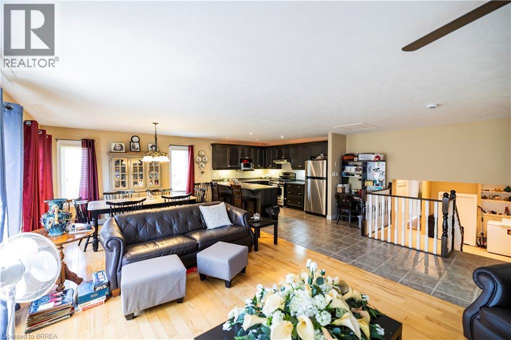 Open-concept living area featuring wood-finish flooring, a dining space with chandelier lighting, a kitchen with dark cabinetry and stainless steel appliances, and a tiled entryway - 100 Mechanic Street W, Waterford, ON - Indoor Photo Showing Living Room
