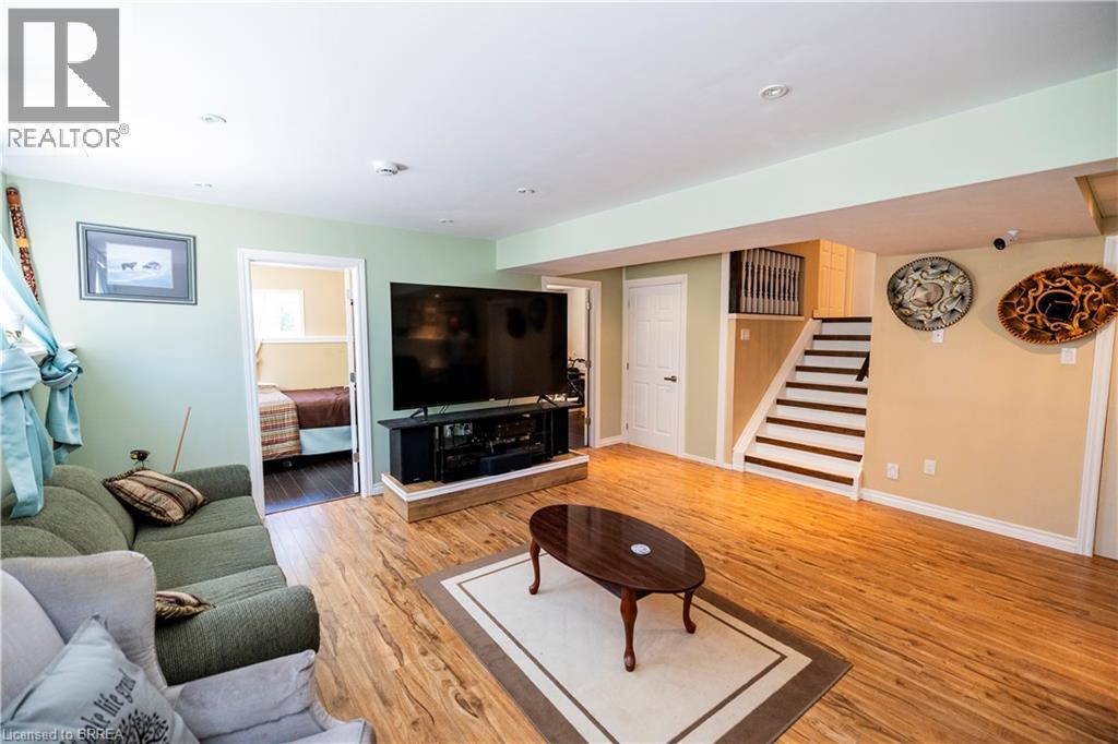 Finished lower level featuring wood-finish flooring, recessed lighting, a built-in media console, a staircase with dark treads, and a white interior door - 100 Mechanic Street W, Waterford, ON - Indoor Photo Showing Living Room