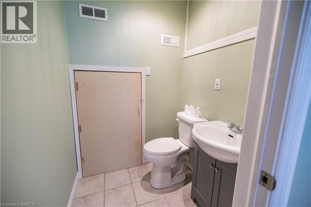 Bathroom featuring light green walls, white crown molding, a white toilet, a white porcelain sink, and a gray vanity cabinet - 100 Mechanic Street W, Waterford, ON - Indoor Photo Showing Bathroom