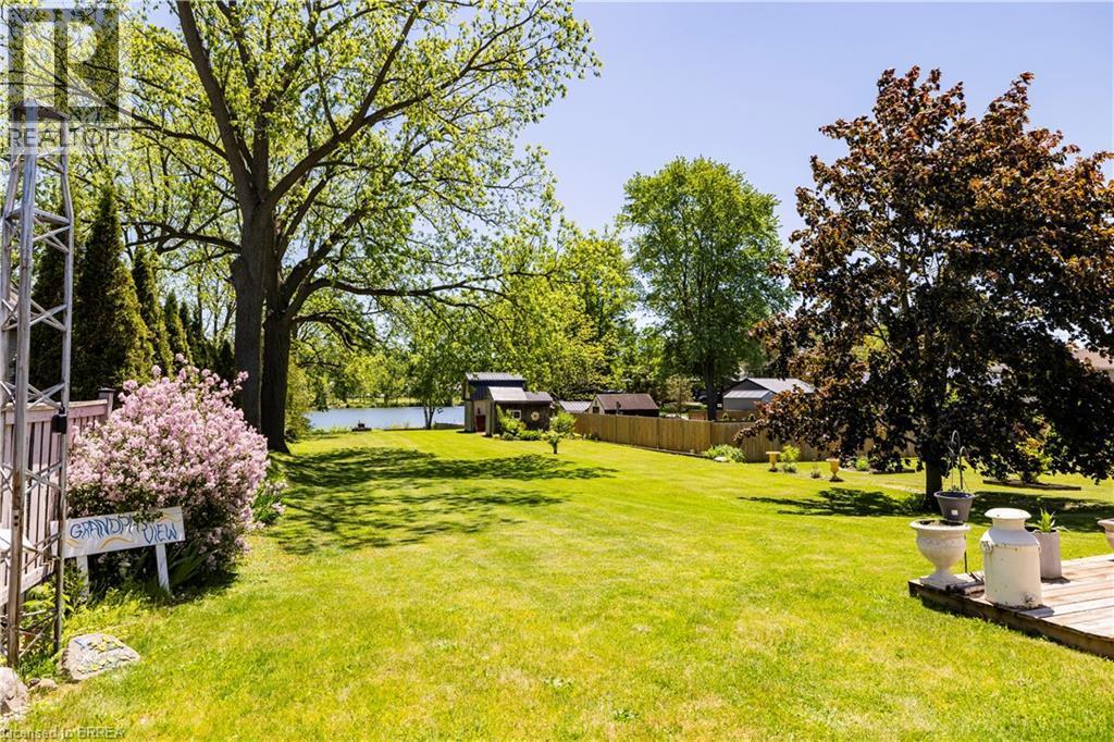 Expansive green lawn with mature trees and a tranquil body of water in the background - 100 Mechanic Street W, Waterford, ON - Outdoor