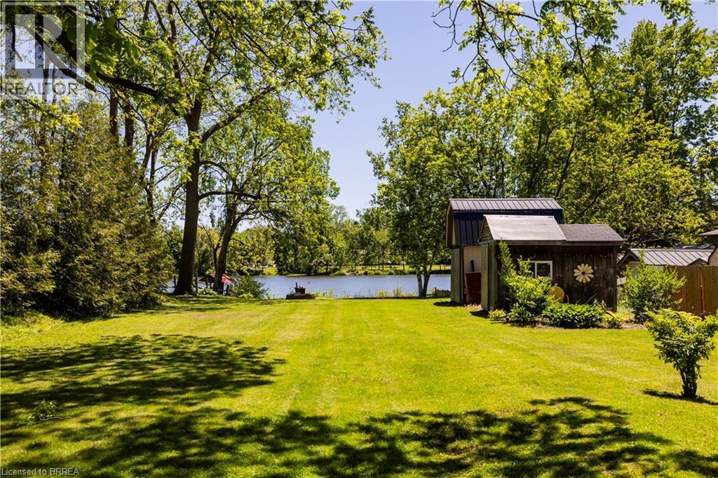 Expansive green lawn extending to a body of water, bordered by mature trees and evergreen shrubs - 100 Mechanic Street W, Waterford, ON - Outdoor