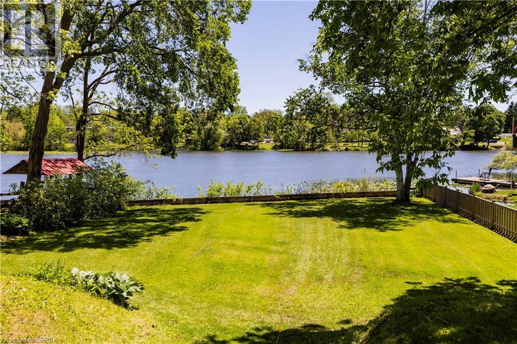 Expansive lakeside property featuring a large grassy lawn, mature shade trees, and a wooden privacy fence - 100 Mechanic Street W, Waterford, ON - Outdoor With Body Of Water With View