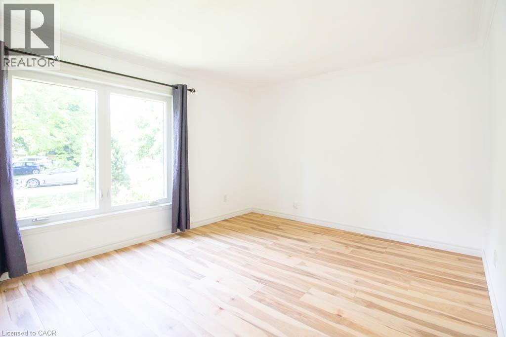 Bright interior room featuring a large double window, natural light, wood-finish flooring, and white walls - 30 Eastvale Place, Hamilton, ON - Indoor Photo Showing Other Room