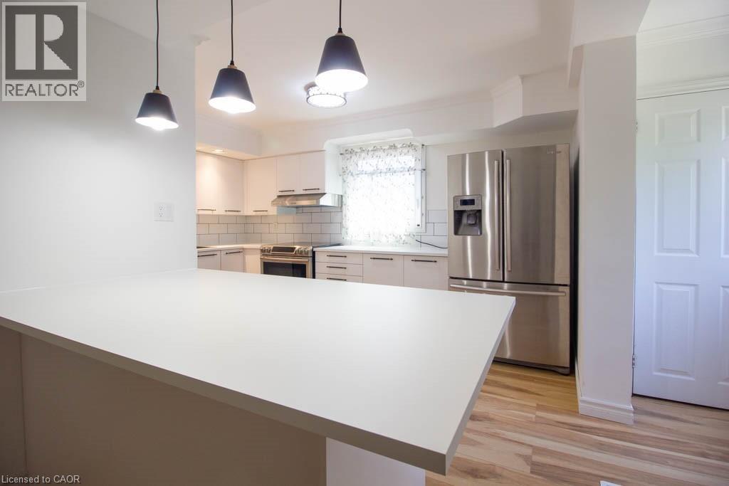 Kitchen featuring a spacious white countertop island, stainless steel refrigerator, white cabinetry, subway tile backsplash, and light wood-finish flooring - 30 Eastvale Place, Hamilton, ON - Indoor Photo Showing Kitchen