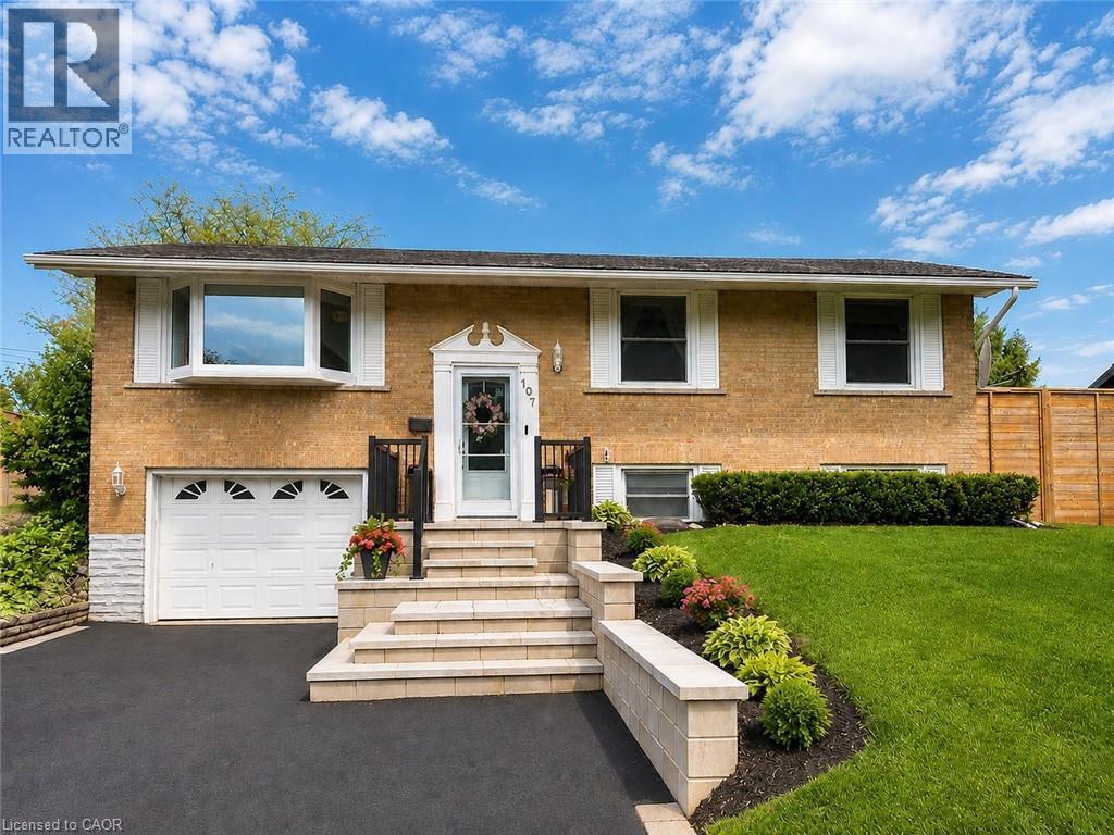 Brick facade residence featuring an attached garage, bay window, landscaped front yard with block retaining walls, and a paved driveway - 107 Rosslinn Road, Cambridge, ON - Outdoor