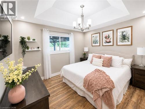 Interior room featuring wood-finish flooring, a tray ceiling with a chandelier, recessed lighting, and a large window with white curtains - 107 Rosslinn Road, Cambridge, ON - Indoor Photo Showing Bedroom