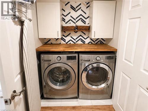Dedicated laundry space featuring a wood-finish countertop, two white upper cabinets, and a chevron pattern accent wall - 107 Rosslinn Road, Cambridge, ON - Indoor Photo Showing Laundry Room