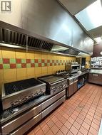 Commercial kitchen featuring extensive stainless steel appliances, a large ventilation hood system, patterned tile backsplash, and durable red-hued tile flooring -