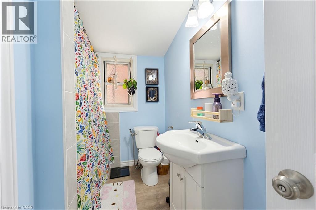 Full bathroom featuring a white pedestal sink vanity with chrome faucet, a wall-mounted mirror with integrated lighting, a toilet, and a tiled shower area - 291 Park Avenue, Brantford, ON - Indoor Photo Showing Bathroom
