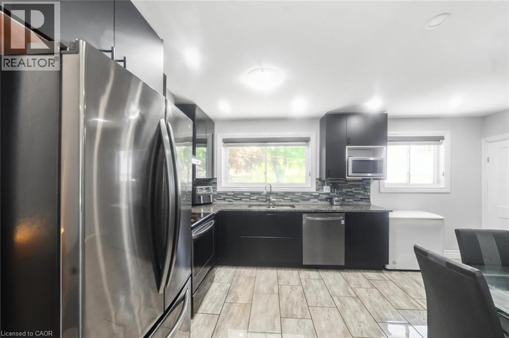 Kitchen featuring stainless steel appliances, dark cabinetry, light-toned tile flooring, dual windows, and a mosaic tile backsplash - 158 Plymouth Road, Kitchener, ON - Indoor Photo Showing Kitchen With Stainless Steel Kitchen With Upgraded Kitchen