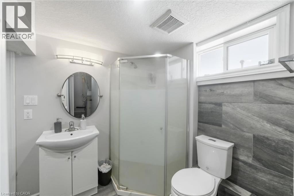 Bathroom featuring a corner shower with frosted glass enclosure, a white vanity with integrated sink, a round wall-mounted mirror, and a wall-mounted light fixture - 158 Plymouth Road, Kitchener, ON - Indoor Photo Showing Bathroom