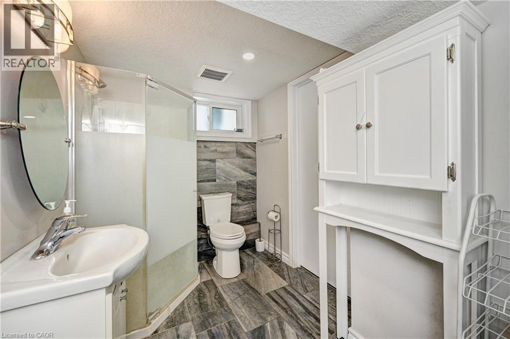 Bathroom featuring a walk-in shower with frosted glass, vanity with an integrated sink, white storage cabinetry, tiled flooring, and a transom window - 158 Plymouth Road, Kitchener, ON