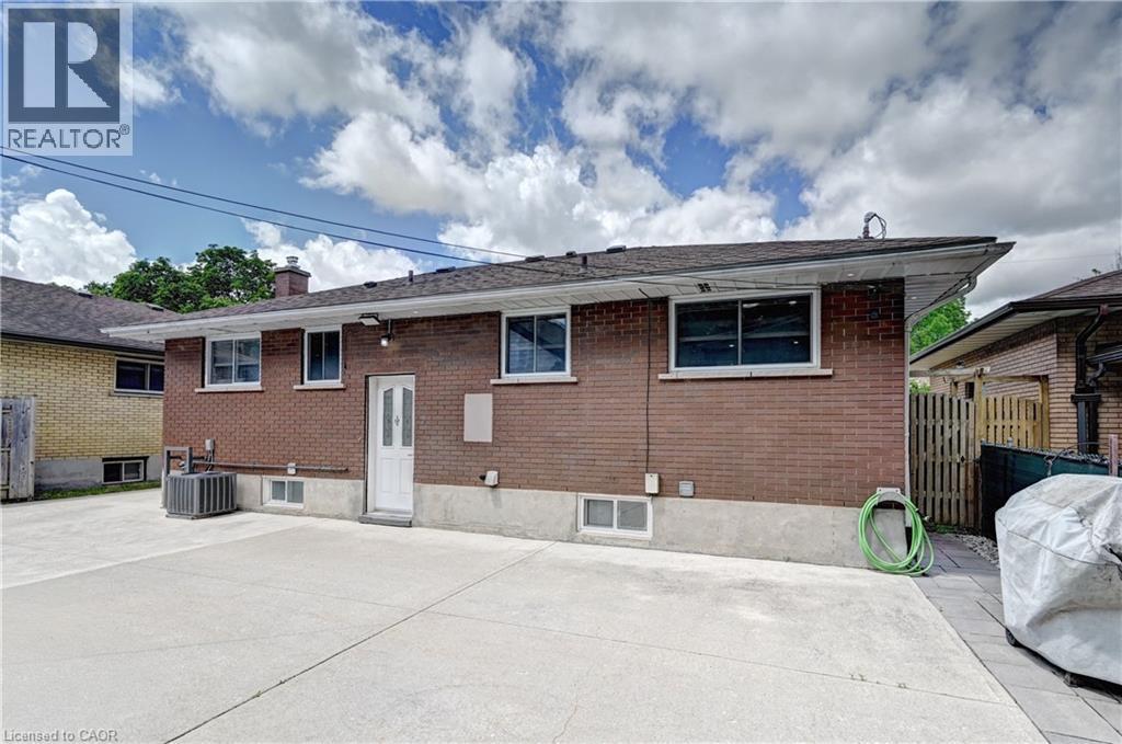 Brick exterior with a white rear entry door, featuring a concrete patio area - 158 Plymouth Road, Kitchener, ON