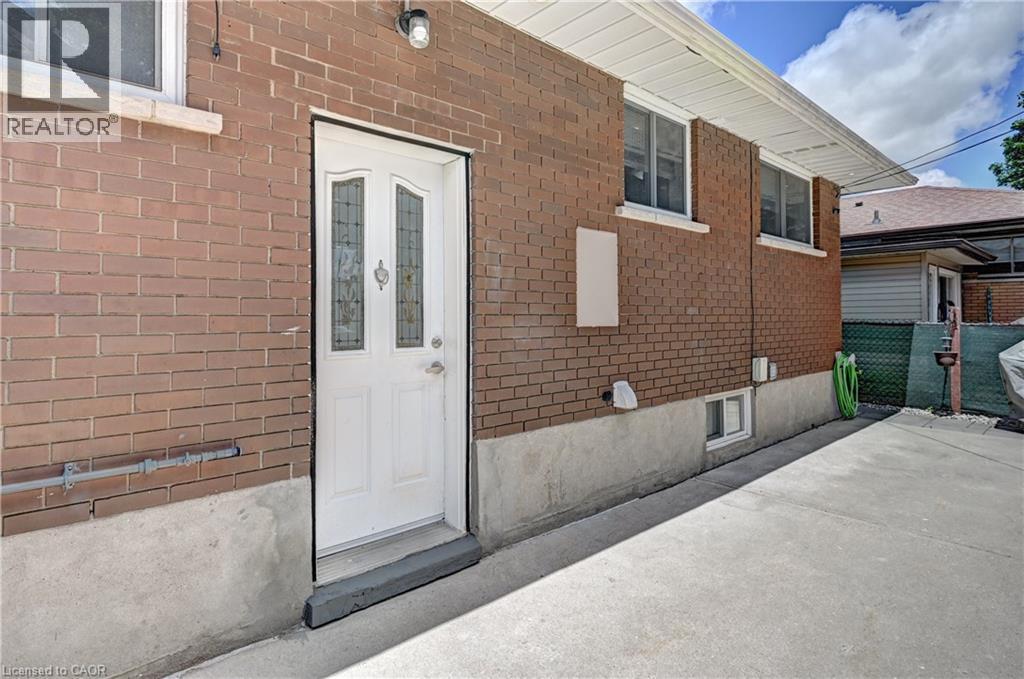 Brick exterior featuring a white entry door with decorative glass inserts, multiple windows, a concrete foundation, and a concrete pathway - 158 Plymouth Road, Kitchener, ON