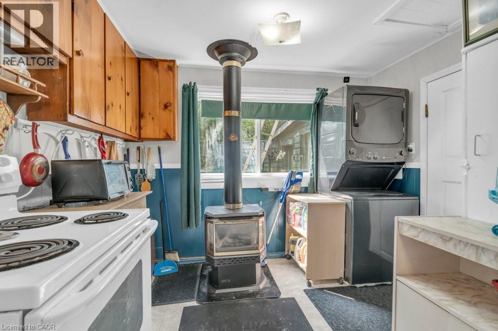 Functional kitchen space featuring a wood-burning stove, natural wood cabinetry, a white electric range, and a stacked washer and dryer unit - 1264 Parkinson Road, Woodstock, ON
