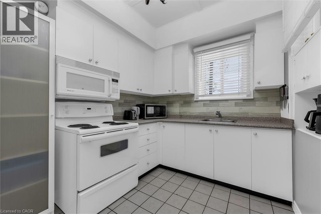 Kitchen featuring white cabinetry, a built-in microwave, an electric range, a stainless steel sink, and a tiled backsplash - 205 Ferguson Avenue S, Hamilton, ON - Indoor Photo Showing Kitchen