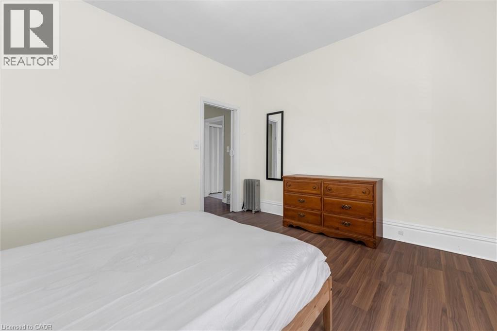 Room featuring wood-finish flooring, white baseboards, and a doorway with a folding door - 205 Ferguson Avenue S, Hamilton, ON - Indoor Photo Showing Bedroom
