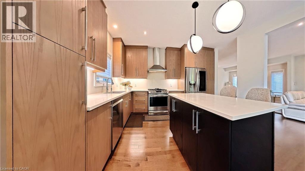 Contemporary kitchen featuring wood-finish cabinetry, stainless steel appliances, and a central island with a white countertop - 63 Ian Ormston Drive, Kitchener, ON - Indoor Photo Showing Kitchen With Upgraded Kitchen
