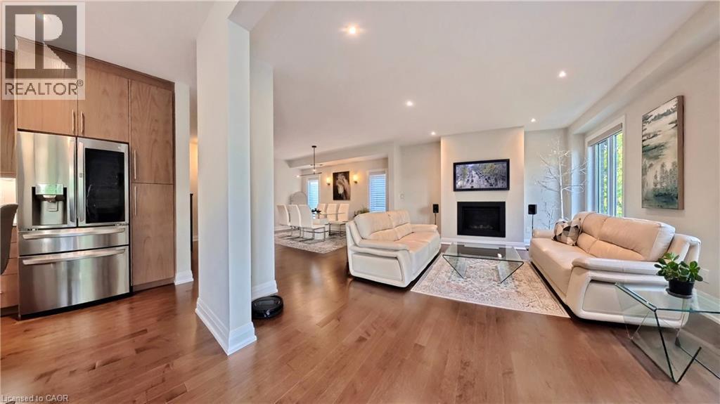 Open concept living space featuring wood-finish flooring throughout, recessed lighting, and a modern fireplace with a wall-mounted display - 63 Ian Ormston Drive, Kitchener, ON - Indoor Photo Showing Living Room With Fireplace