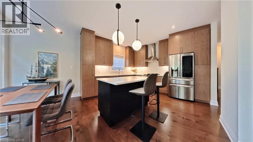 Contemporary kitchen featuring a dark-toned island with a light-toned countertop, wood-finish cabinetry, and stainless steel appliances - 63 Ian Ormston Drive, Kitchener, ON - Indoor