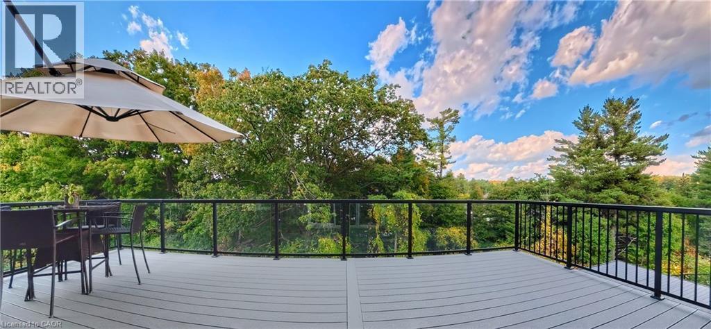 Spacious outdoor deck featuring composite decking, glass panel railings, and surrounding mature trees - 63 Ian Ormston Drive, Kitchener, ON - Outdoor