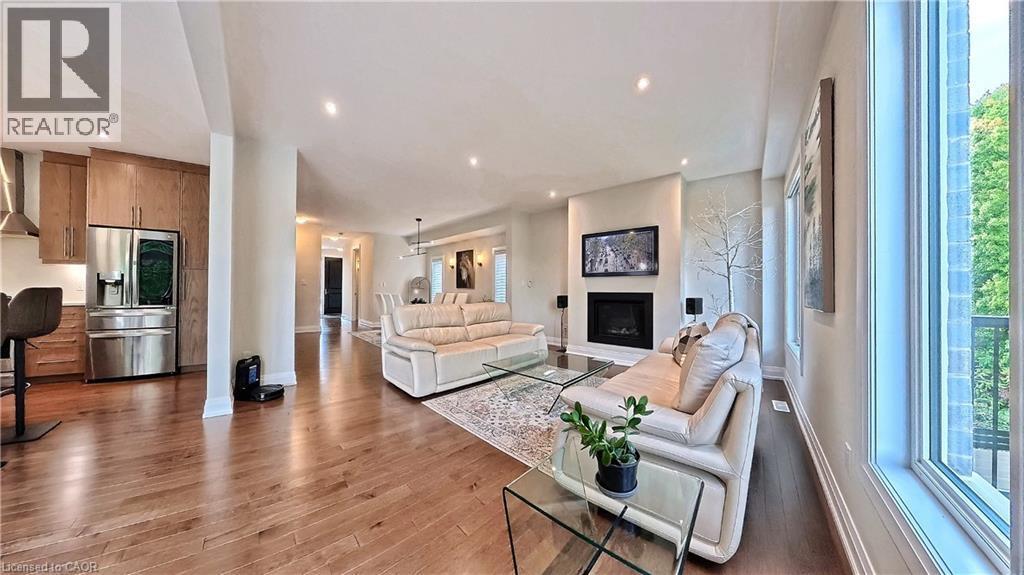 Open-concept living space featuring hardwood flooring, recessed lighting, a built-in fireplace with a wall-mounted display, and large picture windows - 63 Ian Ormston Drive, Kitchener, ON - Indoor Photo Showing Living Room
