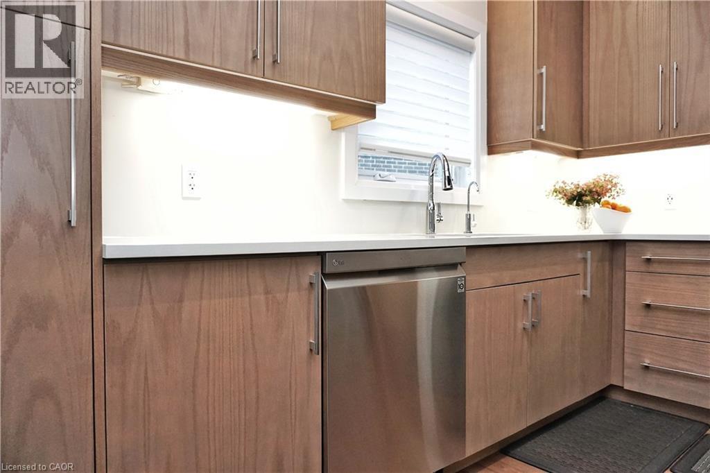 Kitchen featuring wood-finish cabinetry, white countertops, undermount sink with a stainless steel faucet, and an integrated stainless steel dishwasher - 63 Ian Ormston Drive, Kitchener, ON - Indoor Photo Showing Kitchen