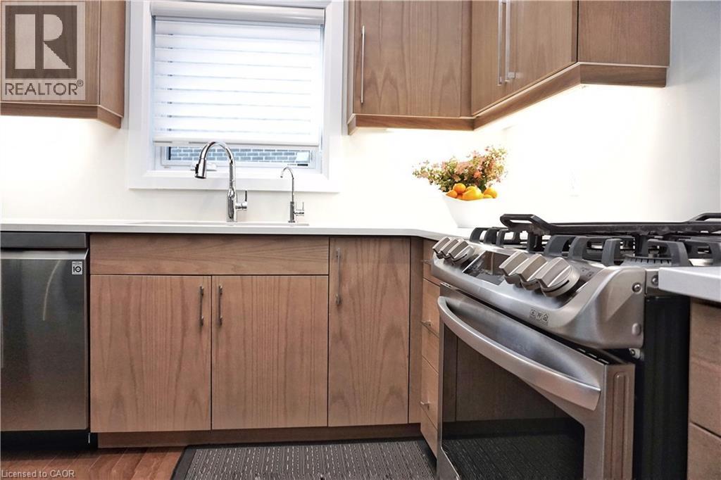 Modern kitchen featuring stainless steel appliances, wood-finish cabinetry, light-toned countertops, and a double basin sink with an arched faucet - 63 Ian Ormston Drive, Kitchener, ON - Indoor Photo Showing Kitchen