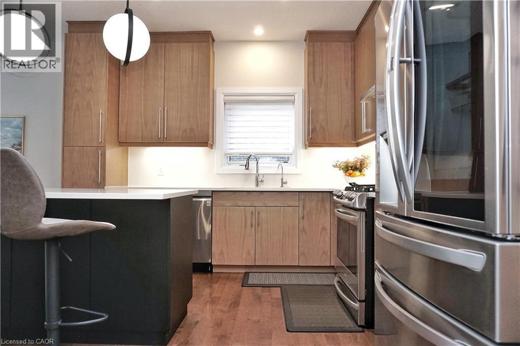 Contemporary kitchen featuring a dark-toned island with a light countertop, wood-finish flooring, and natural wood cabinetry - 63 Ian Ormston Drive, Kitchener, ON - Indoor Photo Showing Kitchen With Upgraded Kitchen