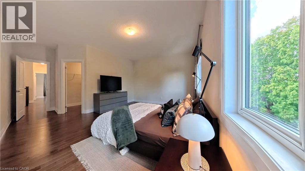 Spacious room featuring rich wood-finish flooring, a large window with white trim, and a built-in closet with shelving - 63 Ian Ormston Drive, Kitchener, ON - Indoor