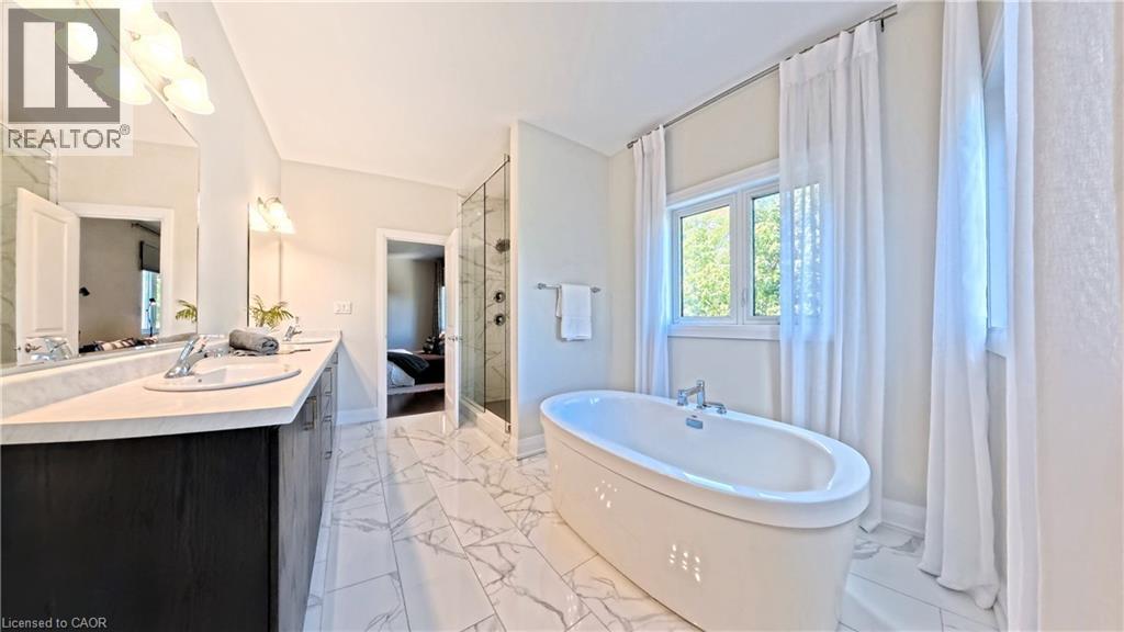 Spacious bathroom featuring a freestanding soaking tub, a large walk-in glass shower, a double vanity with an integrated sink, expansive mirror, and marble-look tile flooring - 63 Ian Ormston Drive, Kitchener, ON - Indoor Photo Showing Bathroom