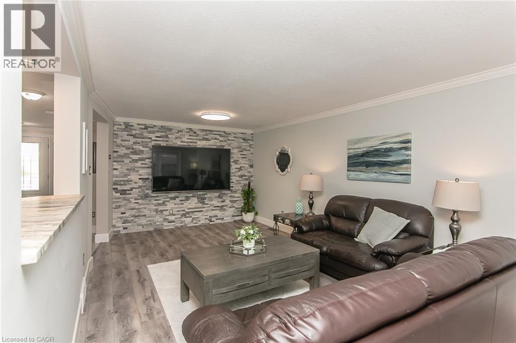 Living area featuring a stone accent wall, wood-finish flooring, recessed lighting, crown molding, and a partial wall with a stone-finish countertop - 529 Chesapeake Crescent, Waterloo, ON - Indoor Photo Showing Living Room