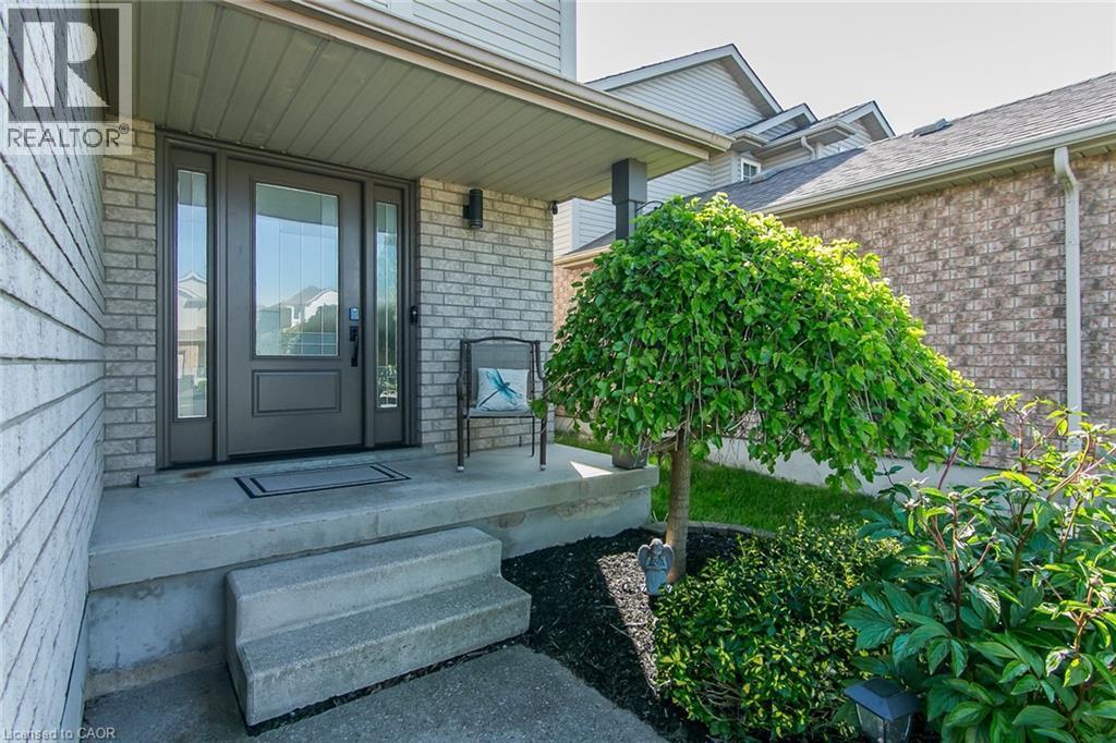 Inviting entryway featuring a dark-paneled door with sidelights, a covered concrete porch, brick facade, and a landscaped garden with a mature tree - 529 Chesapeake Crescent, Waterloo, ON - Outdoor With Deck Patio Veranda