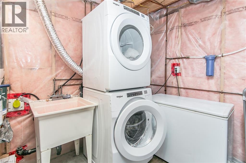 Dedicated laundry area featuring stacked front-load washer and dryer, utility sink, and additional freezer - 529 Chesapeake Crescent, Waterloo, ON - Indoor Photo Showing Laundry Room