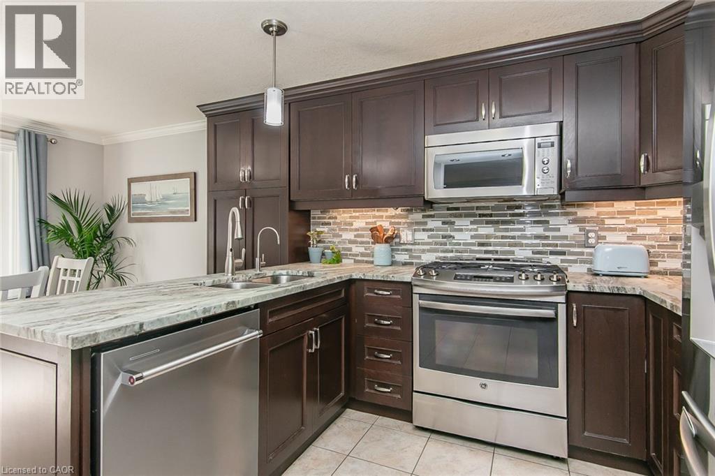 Kitchen featuring dark wood cabinetry, light-toned countertops, tile flooring, stainless steel appliances, and a mosaic tile backsplash - 529 Chesapeake Crescent, Waterloo, ON - Indoor Photo Showing Kitchen With Double Sink With Upgraded Kitchen