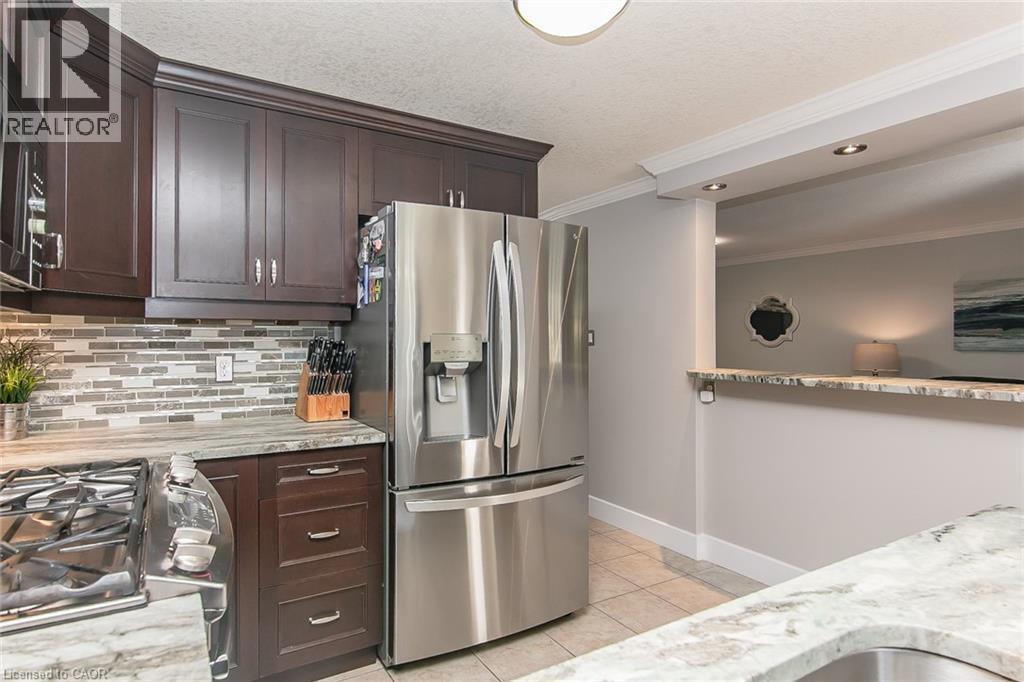 Stainless steel refrigerator and gas range, dark wood cabinetry, tile backsplash, and light-toned countertops - 529 Chesapeake Crescent, Waterloo, ON - Indoor Photo Showing Kitchen
